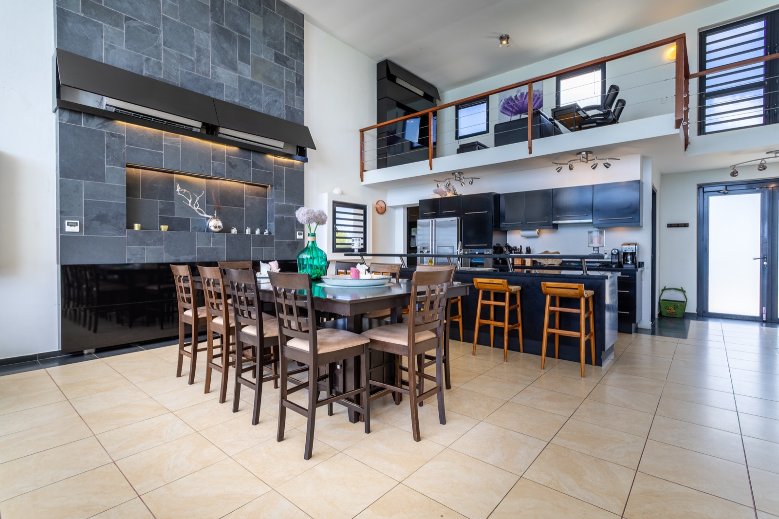 Luxury Bonaire villa great room with open-plan kitchen and dining area, featuring a double-height ceiling, large slate accent wall, and mezzanine loft.